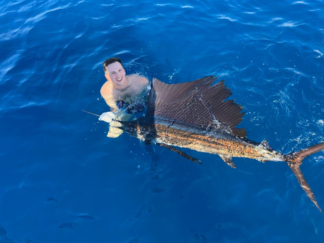 Angler swimming with a sailfish in deep blue Pacific waters
